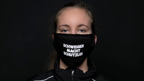 Symbolbild Opferschutz vor sexualisierter Gewalt: Eine junge Frau trägt eine Maske mit dem Schriftzug "Schweigen macht schutzlos"