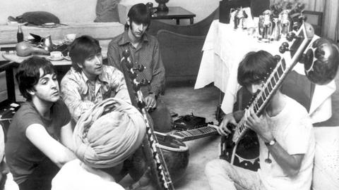 George Harrison nimmt Sitar-Unterricht in Neu Delhi, während Paul McCartney, John Lennon und Ringo Starr zuschauen.