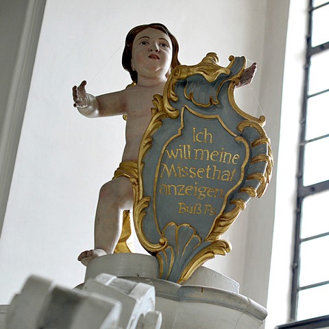 Eine Engelsfigur über einem Beichtstuhl hält eine Tafel mit dem Buß-Psalm "Ich will meine Missethat anzeigen".