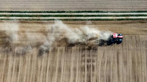 Bayern, Kleinpinning: Ein Landwirt wirbelt mit seinem Traktor beim Bearbeiten eines Feldes Staub auf (Luftaufnahme mit Drohne).