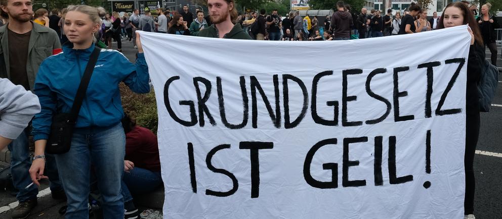  Sachsen, Chemnitz: Zuschauer stehen vor dem Konzert unter dem Motto «#wirsindmehr» auf einer Straße am Parkplatz vor der Johanniskirche und halten ein Transparent mit der Aufschrift "Grundgesetz ist geil". Bei dem Konzert wollten unter anderem Marteria und Casper, Kraftclub und die Toten Hosen auftreten. Die Bands wollen damit ein Zeichen gegen Rassismus, Ausländerfeindlichkeit und Gewalt setzen.