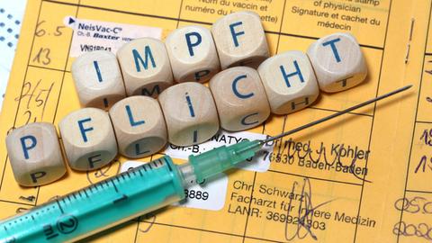 Eine Coronaspritze, Impfspritze liegt neben dem Wort Impfpflicht auf einem Impfpass,