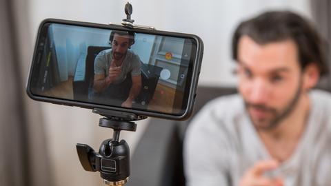ILLUSTRATION - Ein Mann sitzt am 04.12.2018 in einer Wohnung in Hamburg auf einer Couch und nimmt ein Video mit seinem Smartphone auf (gestellte Szene).
