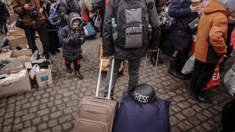 Ein Journalist mit Schutzhelm im Gepäck geht an Geflüchteten vorbei zur ukrainisch-polnischen Grenze.