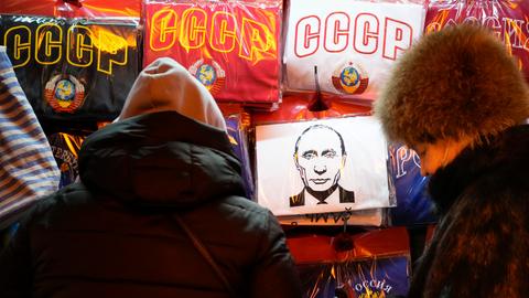 Frauen betrachten T-Shirts, auf denen unter anderem die Buchstaben der UdSSR und der russische Präsident Putin abgebildet sind, in einem Souvenirladen.