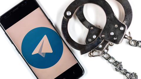 Neben einem Smartphone mit dem Logo von Telegram liegen Handschellen.