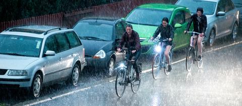 22.04.2018, Niedersachsen, Göttingen: Radfahrer fahren bei kurzem Starkregen und Gewitter an parkenden Autos vorbei.