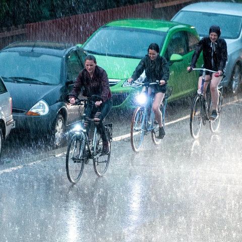 22.04.2018, Niedersachsen, Göttingen: Radfahrer fahren bei kurzem Starkregen und Gewitter an parkenden Autos vorbei.