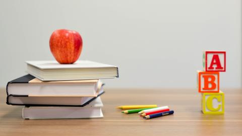 Schulbücher, Stifte und ein Apfel liegen auf einem Tisch