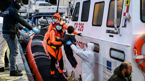 Besatzungen der italienischen Küstenwache helfen einem Kind beim Verlassen eines Rettungsbootes im Hafen von Roccella Jonica.