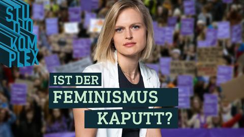 Die Hostin ist im Vordergrund und blickt direkt in die Kamera. Hinter ihr sieht man verschwommen eine Demonstration mit vielen Menschen mit lila farbenen Bannern