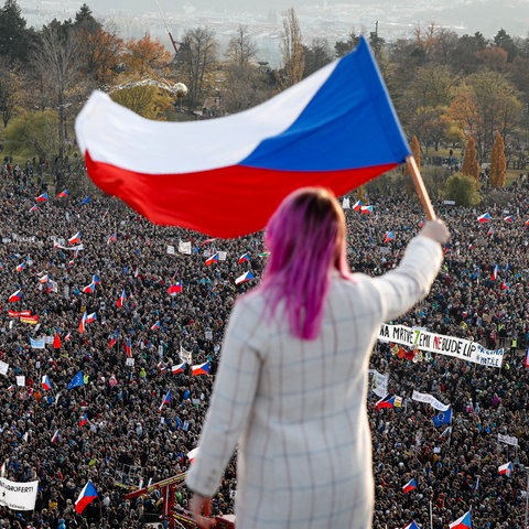 Eine Frau winkt bei einer Großkundgebung gegen die Regierung eine tschechische Flagge aus einem Dach (2019)