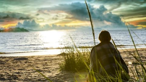 Frau sitzt am Strand.