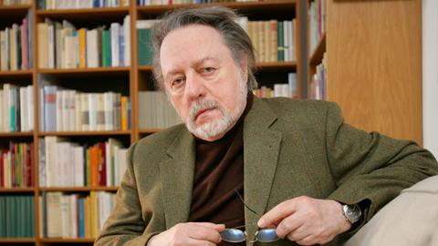 Ror Wolf sitzt in seiner Wohnung vor einem Bücherregal.