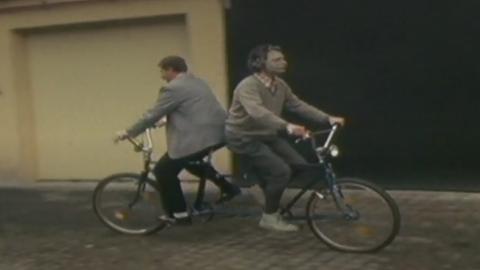 Zwei Männer fahren in unterschiedlicher Sitzposition auf einem Fahrrad
