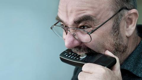 Ein Mann beißt vor Wut in sein Telefon.