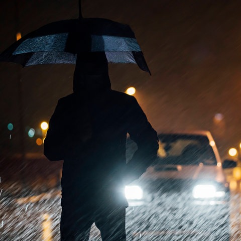 Mann steht bei Nacht im Regen vor Auto
