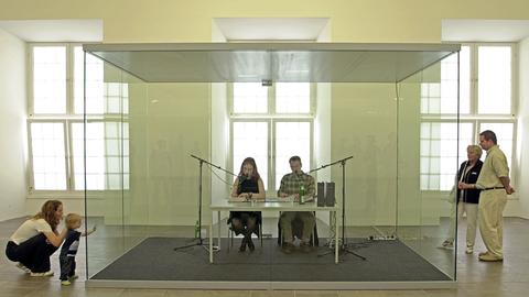 In einem Glaskasten in der Kasseler Kunsthalle Fridericianum sitzen zwei documenta-Mitarbeiter und lesen abwechselnd Jahreszahlen vor. 