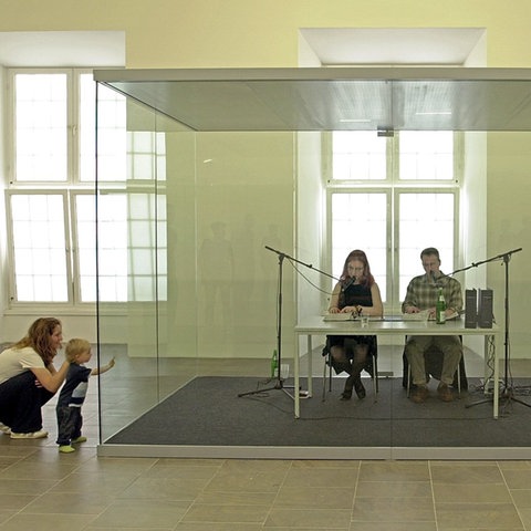 In einem Glaskasten in der Kasseler Kunsthalle Fridericianum sitzen zwei documenta-Mitarbeiter und lesen abwechselnd Jahreszahlen vor. 