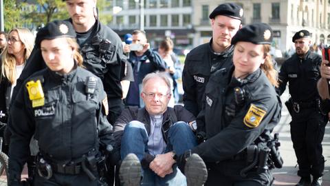 Jesuiten-Pater Jörg Alt wird nach einer Klebe-Aktion von der Polizei abtransportiert.