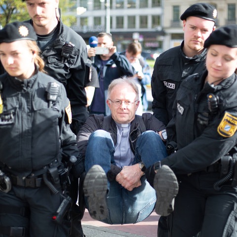 Jesuiten-Pater Jörg Alt wird nach einer Klebe-Aktion von der Polizei abtransportiert.