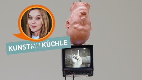 Installation von Bruce Nauman: Ein umgekehrter menschlicher Kopf aus Wachs hängt über einem Monitor, der eine Hand mit ausgestrecktem Mittelfinger zeigt.