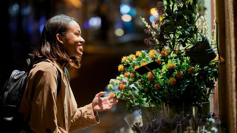 Frau steht vor einem Blumenladen und freut sich