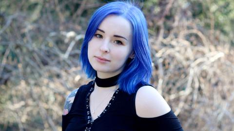 Junge Frau mit blauen Haaren und einem schulterfreien schwarzen Oberteil