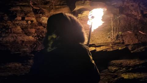 Gestalt mit einer Jacke mit Fellkapuze von hinten hält eine brennende Fackel