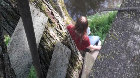 Mädchen sitzt auf Baum und schaut ins Wasser 