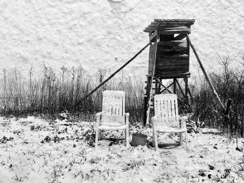 Impressionen aus dem Vogelsberg: zwei weiße Plastikstühle vor einem schiefen Hochstand, alles leicht Schnee bedeckt