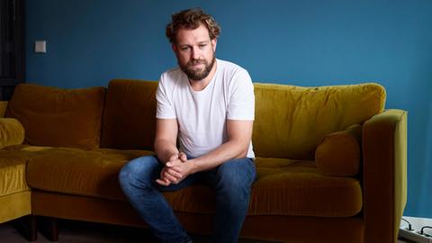 Der Tenor Julian Pregardien sitzt barfuß auf seinem Sofa