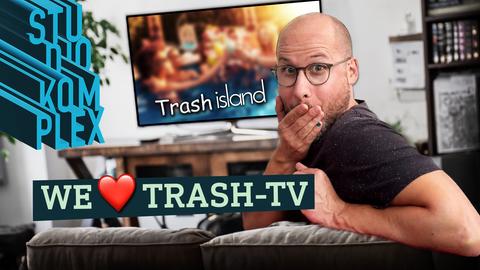 Host David sitzt auf der Couch und grinst verstohlen in die Kamera. Hinter ihm läuft "Trash island"