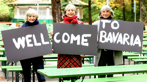 Drei Frauen halten Schilder mit Well Come to Bavaria hoch