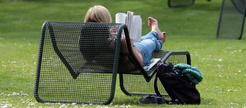 Eine junge Frau genießt den warmen Frühlingstag mit einem Buch im Liegestuhl im Palmengarten.