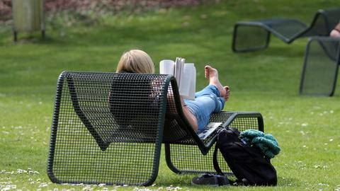 Eine junge Frau genießt den warmen Frühlingstag mit einem Buch im Liegestuhl im Palmengarten.